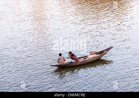 Einheimische Fischer fischen mit Netzen von einem kleinen hölzernen Ruderboot im Hooghly River, Serampore, in der Nähe von Kalkutta, West-Bengal, Indien im Abendlicht Stockfoto