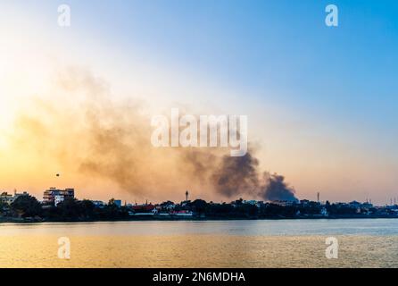 In der Dämmerung steigt dichter, verschmutzender Rauch am Ufer des Hooghly River auf, der den Smog und die schlechte Luftqualität in der Nähe von Kalkutta, Westbengalen, Indien, verstärkt Stockfoto