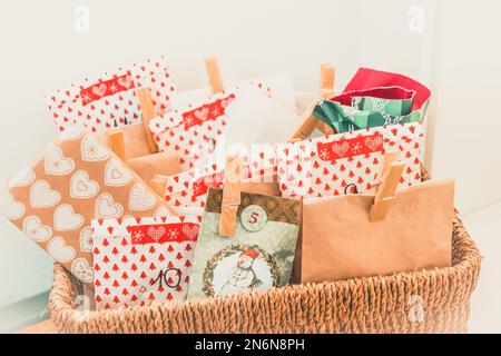 Handgefertigter Adventskalender mit bunten Papiertaschen und Aufklebern in einem gewebten Korb Stockfoto