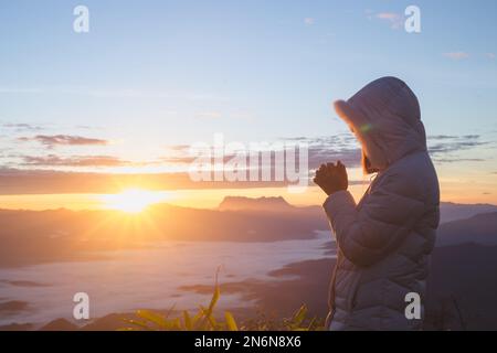 Bete am Morgen, Frau betet mit Händen zusammen am Morgen Sonnenaufgang Hintergrund. Stockfoto