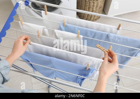 Eine Frau, die saubere Wäsche an einen Wäscheständer in der Halle hängt Stockfoto