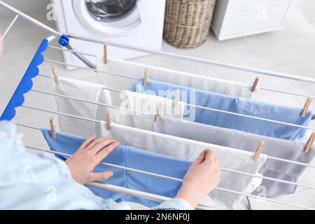 Eine Frau, die saubere Wäsche an einen Wäscheständer in der Halle hängt Stockfoto