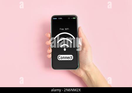 Frau, die sich mit einem Mobiltelefon auf pinkfarbenem Hintergrund mit WLAN verbindet, Nahaufnahme Stockfoto