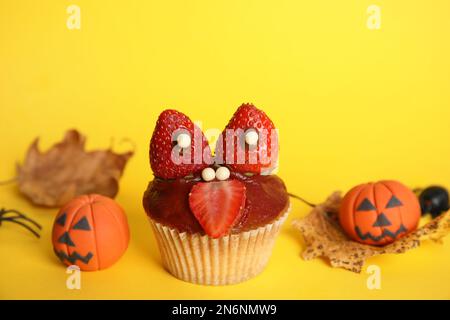 Köstlicher Cupcake dekoriert als Monster auf gelbem Hintergrund. Halloween-Leckerbissen Stockfoto