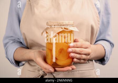 Eine Frau mit einem Glas eingelegter Pfirsiche auf hellem Hintergrund, Nahaufnahme Stockfoto