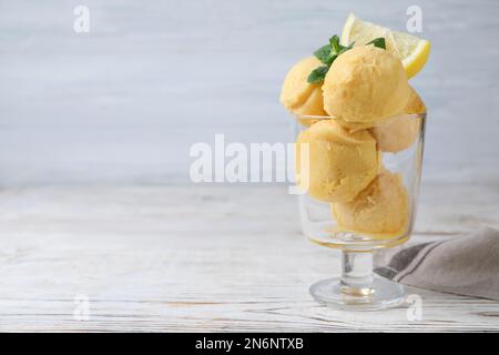 Leckeres Zitroneneis in der Dessertschüssel auf einem weißen Holztisch, Platz für Text Stockfoto