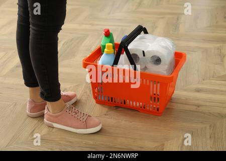 Frau und Warenkorb mit Haushaltswaren auf Holzboden, Nahaufnahme Stockfoto