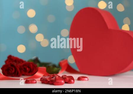 Herzförmige Schokoladenbonbons auf einem rosafarbenen Tisch vor verschwommenem Licht. Valentinstag-Feier Stockfoto