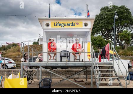 2 Rettungsschwimmer sitzen vor der Rettungsschwimmerstation am Swanage Beach in Dorset und beobachten den Strand und das Meer, um die Menschen zu schützen Stockfoto