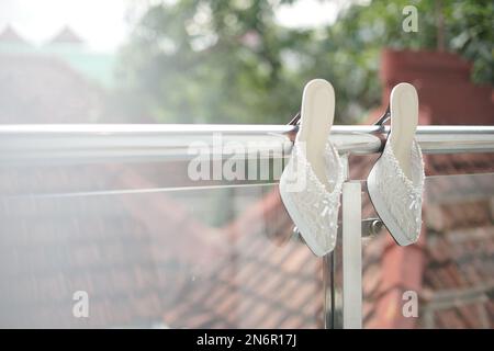 Ein Paar Brautschuhe, die für die Hochzeitszeremonie am Balkonzaun hängen Stockfoto