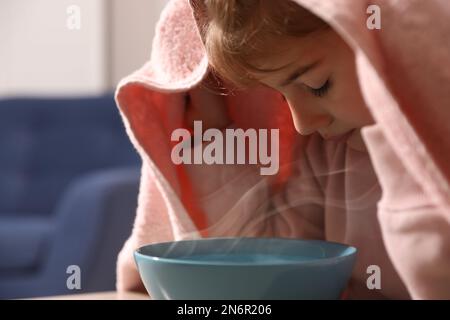 Kleines Mädchen, das den Kopf mit einem Handtuch bedeckt und drinnen Dampf inhaliert, Nahaufnahme Stockfoto