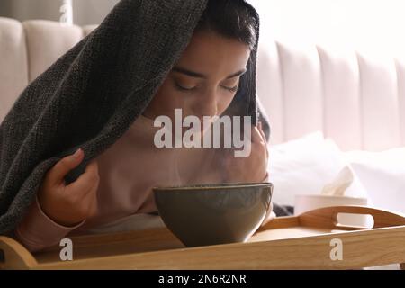 Eine Frau mit Karomuster, die drinnen über der Schüssel inhaliert Stockfoto