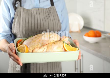Eine Frau, die eine Pfanne mit rohem Hühnchen und Orangen in der Küche hält Stockfoto