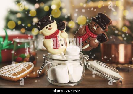 Lustige Schokoladen-Schneemänner-Süßigkeiten in einem Glas voller Marshmallows auf einem Holztisch, Nahaufnahme Stockfoto