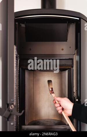 Mann, der Pelletofen mit Bürste reinigt Stockfoto