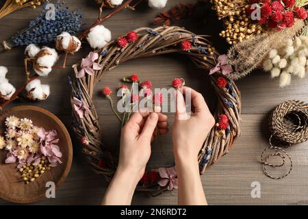 Florist macht Kranz mit getrockneten Blumen auf einem Holztisch, Draufsicht Stockfoto