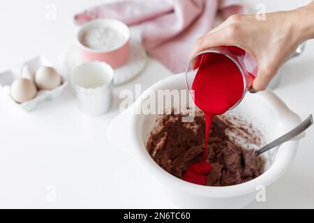 Person, die roten Samtkuchen macht und dem Teig rote Lebensmittelfarbe hinzufügt Stockfoto