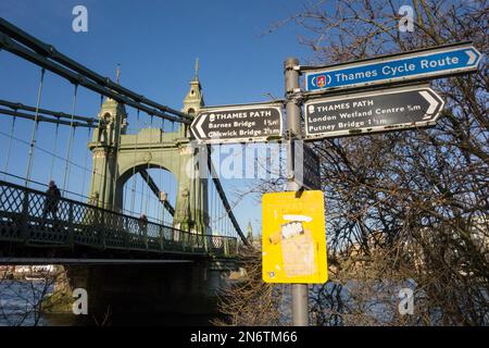 Beschilderung zum Thames Cycle Path und eine noch immer fest geschlossene Hammersmith Bridge, die repariert wird und auf die Planungsgenehmigung für eine neue Straßenoberfläche wartet Stockfoto