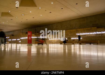 Eine Frau, die allein mit einem roten Hut in den Galerien des Louvre in Paris sitzt, mit Menschen, die sich bewegen und Licht um sie herum haben. Leichte Sätze auf dem Flügel. Stockfoto