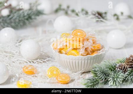 Schüssel mit Süßigkeiten in Form von Orange- und Zitronenscheiben, einzeln in Folie verpackt, auf weißem Hintergrund mit weihnachtsdekoration Stockfoto