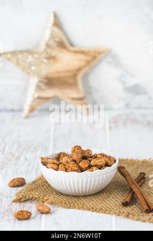 Schüssel mit süßen kandierten Mandeln auf weißem rustikalem Holzhintergrund, ein Holzstern im Hintergrund, weihnachtsdekoration, vertikal Stockfoto