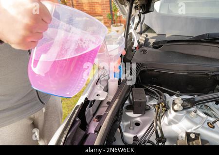 Flacher Fokus der Scheibenwaschflüssigkeit, die vom Besitzer in den Kunststoffbehälter eines beliebten SUV gegossen wird. Stockfoto