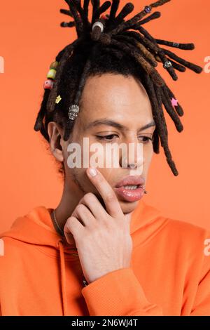 Porträt eines multirassischen Mannes mit Dreadlocks, die das Gesicht berühren, während sie auf korallischem Hintergrund denken Stockfoto