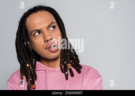 Porträt eines durchdachten Multirassenmannes in pinkfarbenem Hoodie, der isoliert auf Grau wegsieht Stockfoto