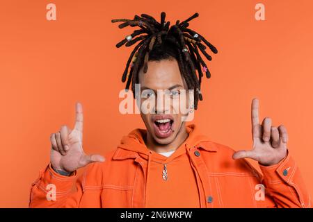 Porträt eines tätowierten multirassischen Mannes mit Dreadlocks, der in die Kamera schaut und auf Korallenhintergrund isolierte Geste zeigt Stockfoto