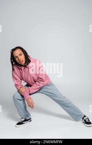 Ein Mann mit mehreren Rassen und durchbohrten Einstichen, mit Dreadlocks, die sich posieren, während sie auf grau in die Kamera schauen Stockfoto