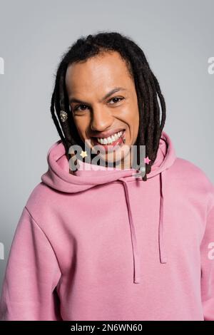Porträt eines glücklichen multirassischen Mannes mit Dreadlocks, die auf grau isoliert lächeln Stockfoto