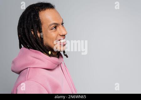 Porträt eines fröhlichen multirassischen Mannes mit lächelnden und wegschauenden Dreadlocks isoliert auf Grau Stockfoto