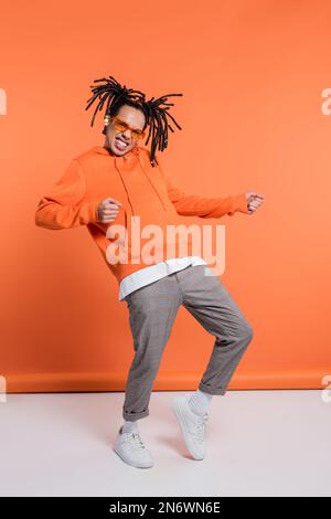 Aufgeregter Mann aus verschiedenen Rassen im Hoodie, trägt eine stilvolle Sonnenbrille und tanzt auf Korallenhintergrund Stockfoto