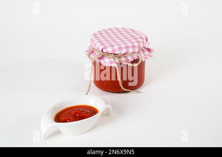 Traditionelle hausgemachte Chili-Tomaten-Sauce in Glasgefäß und kleinem Topf isoliert auf weißem Hintergrund. Stockfoto