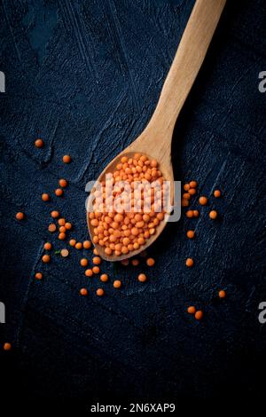 Getrocknete rote Linsen in einem Holzlöffel auf dunklem Hintergrund. Kopierraum. Draufsicht. Stockfoto