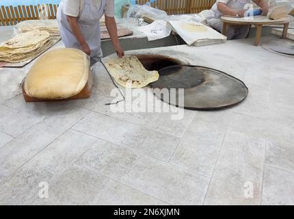 Ich backe das Brot in Tandoor. Die Frau rollt Teig aus. Traditionelle flache Kuchen machen. Brotherstellung in traditioneller Bäckerei Stockfoto