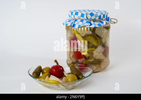Gemischte Gewürzgurken, Sauerkraut, Pfeffer, Tomaten- und Gurkenpickles in Glasgefäß und Teller, isoliert auf weißem Hintergrund. Stockfoto