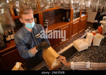 Der Kellner gibt dem Gast im Restaurant eine Bestellung zum Mitnehmen. Gastronomie während der Coronavirus-Quarantäne Stockfoto