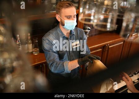 Der Kellner gibt dem Gast im Restaurant eine Bestellung zum Mitnehmen. Gastronomie während der Coronavirus-Quarantäne Stockfoto