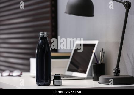 Moderne schwarze Thermosflasche auf dem Tisch im Büro Stockfoto