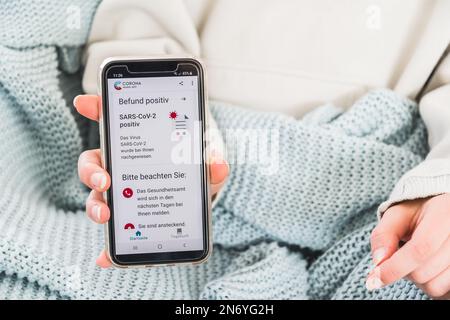 Deutschland - März 27. 2021: Offizielle deutsche Corona Warning App mit positivem Covid-19-Testergebnis auf einem Smartphone, das von einer Frau gezeigt wird. Stockfoto