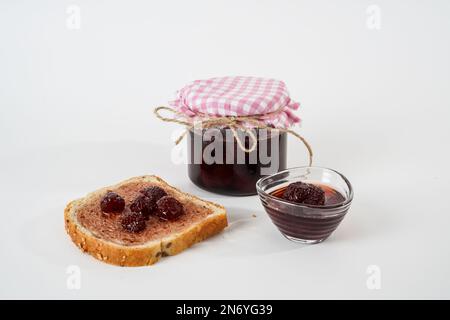 Hausgemachte Erdbeermarmelade, Weithalsgefäß, kleine Schüssel und eine Scheibe Brot mit isolierter Marmelade auf weißem Hintergrund. Stockfoto