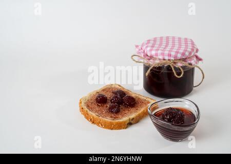 Hausgemachte Erdbeermarmelade, Weithalsgefäß, kleine Schüssel und eine Scheibe Brot mit isolierter Marmelade auf weißem Hintergrund. Stockfoto