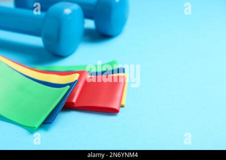 Fitness-Elastikbänder und Kurzhanteln auf hellblauem Hintergrund, Nahaufnahme. Platz für Text Stockfoto