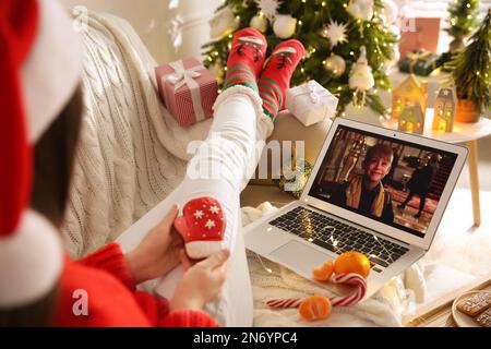 MYKOLAIV, UKRAINE - 25. DEZEMBER 2020: Frau mit Lebkuchen, die sich einen Film „Home Alone“ auf einem Laptop im Haus ansieht, Nahaufnahme. Gemütliche Winterurlaubsatmosphäre Stockfoto