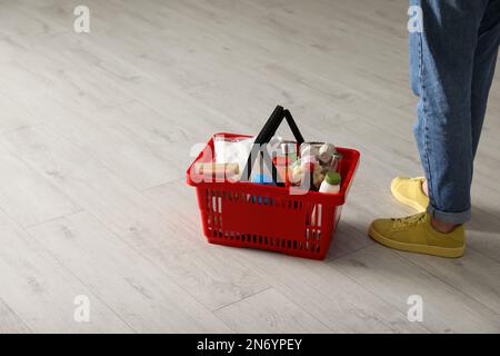 Frau und Einkaufskorb mit Lebensmitteln auf weißem Holzboden, Nahaufnahme Stockfoto
