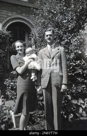 1940er Jahre, historisch, ein gut gekleidetes, aristokratisches englisches Paar, das draußen für ein Foto steht, die Dame, die ihr Baby hält, England, Großbritannien. Gentlemn trägt eine karierte Jacke, Krawatte und Streifenmuster. Stockfoto