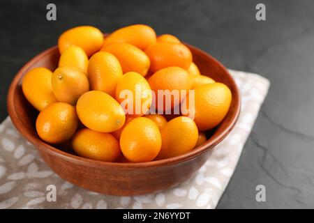 Frische reife Kumquats in Schüssel auf schwarzem Tisch, Nahaufnahme Stockfoto