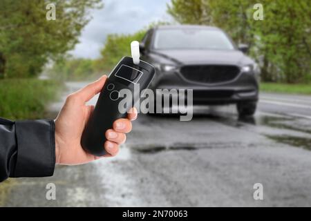 Polizeibeamter mit Atemgerät und Auto auf der Straße. Alkoholkonsum während der Fahrt Stockfoto