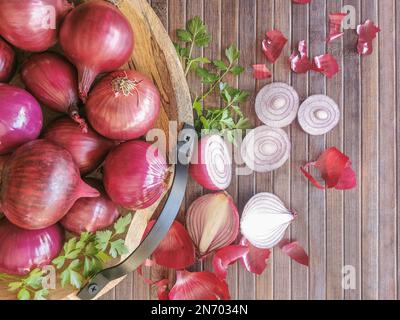 Foto-Komposition mit ganzen Zwiebeln in traditioneller Holzschüssel, Hintergrund mit Holztisch und geschnittenen Zwiebeln und Petersilienzweig... Stockfoto